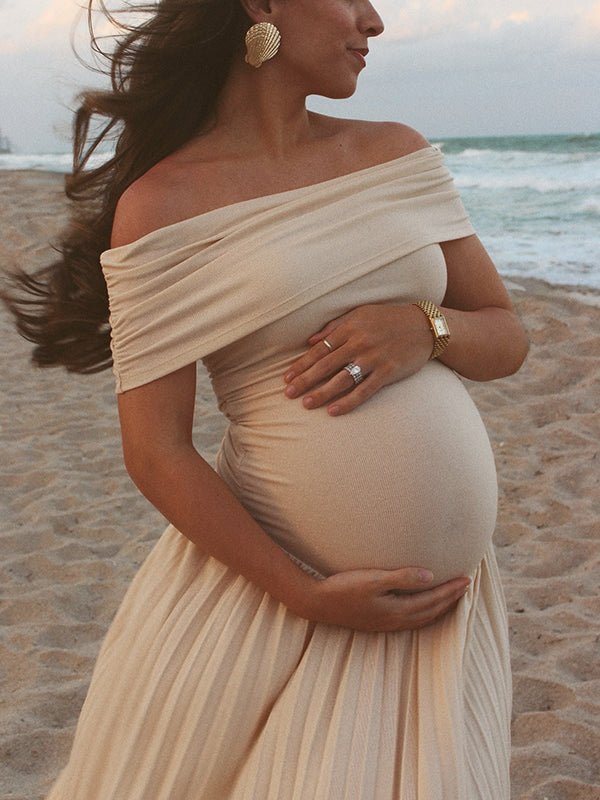 Apricot maternity maxi dress with off-shoulder neckline, pleated skirt, and flowy silhouette, designed for beach photoshoot.
