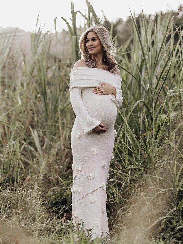 White maternity maxi dress with off-shoulder 3D flowers, backless design, and mermaid bodycon silhouette, designed for maternity photoshoot.